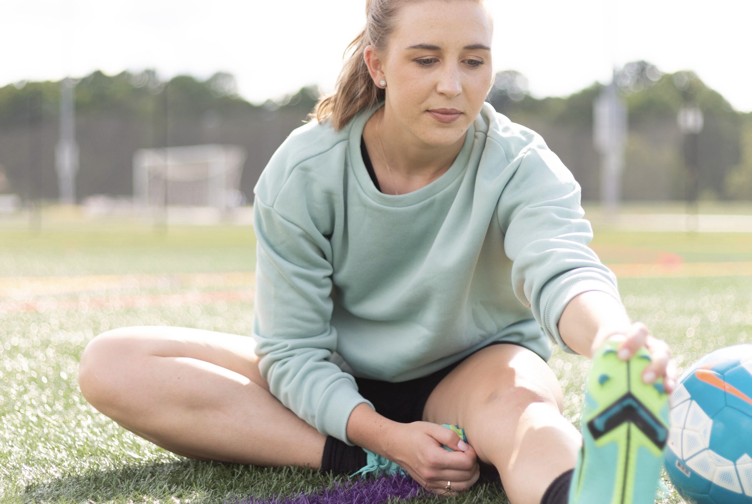 Sports dietitian wearing teal sweatshirt stretching on a soccer field